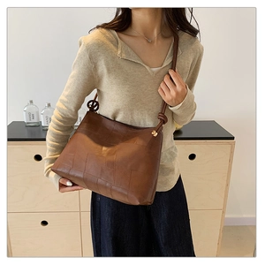 Dark brown faux leather tote bag with knot strap detail and golden hardware on model