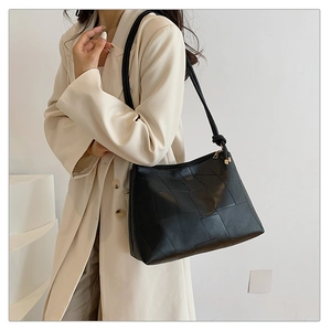 Minimalist black patchwork leather tote bag for women worn over shoulder with white suit