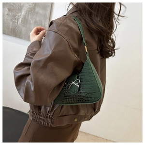 Détail du sac bandoulière vert croco avec nœud en métal argenté porté sur l'épaule du modèle