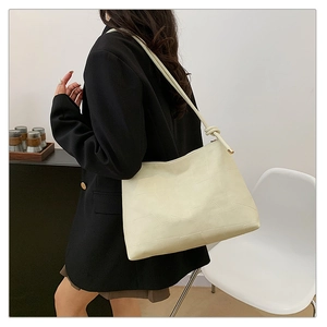 Detail of cream white shoulder bag featuring irregular embossed texture and knot strap
