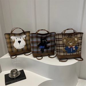 Three checkered tweed tote backpacks with cartoon patches displayed on a white step