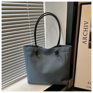 Close-up of blue denim tote bag with black long shoulder straps and metal eyelet details