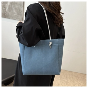 Close-up of blue denim tote bag featuring a unique silver-white rope handle and metal knot detail