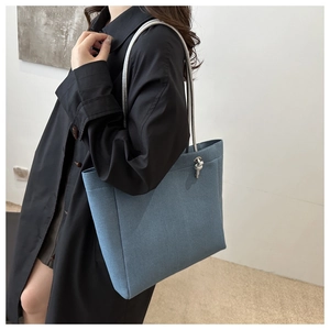 Close-up of blue denim tote bag with silver rope straps and knotted metallic pendant detail