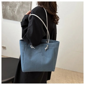 Detail of light blue denim tote bag with silver rope straps and knot decoration