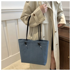 Detail of blue denim tote bag featuring black rope straps and sturdy fabric texture
