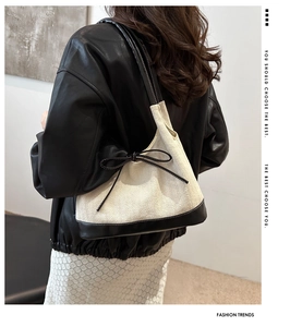 Detail of a chic beige herringbone bucket bag with black leather trim and bow accent
