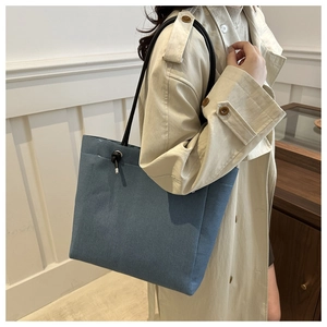 Detail of denim tote bag showing blue fabric texture and black rope handle with metal hardware