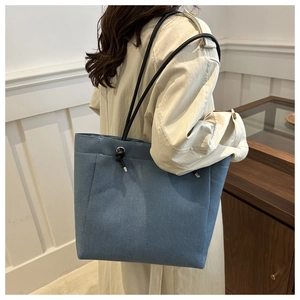 Blue denim tote bag with black shoulder strap and metal hardware detail shown on model
