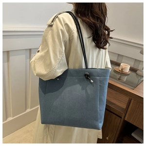 Blue denim tote bag with black rope handles worn by a model in a modern home interior