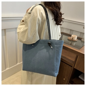 Close-up of denim tote bag with black rope strap knot on beige trench coat