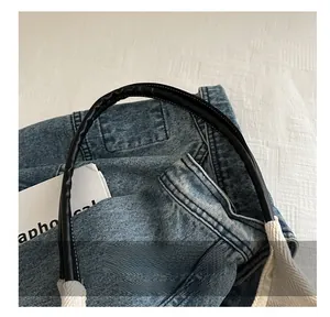 Detail of blue denim handbag featuring black round handles and white cotton webbing strap