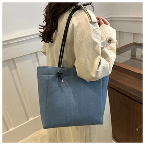 Detail of light blue denim tote bag with black rope straps shown on a model