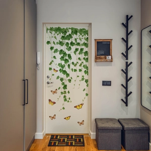 Detailed view of hanging green leaves and colorful butterfly wall stickers on a white door
