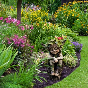 Cute tree spirit garden gnome statue with leaf crown on stump in a floral yard
