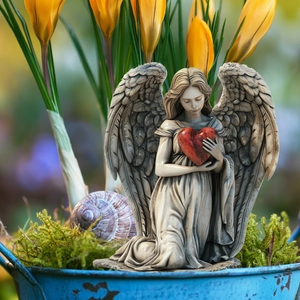 Close-up of kneeling angel figurine with red heart in a garden moss pot with flowers