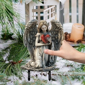 Detail of kneeling angel garden stake holding a red heart in a snowy winter scene