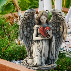 Detailed close-up of a kneeling angel garden statue holding a red heart in the garden