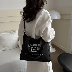 Grand sac fourre-tout noir avec texte blanc, porté par un mannequin dans un salon chic
