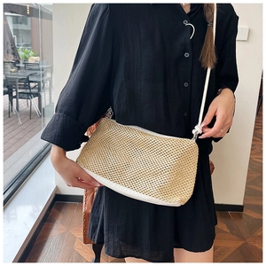 Close-up of a woven straw crossbody bag with white leather straps on a black dress