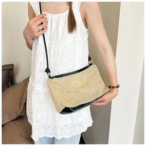 Close-up of straw crossbody bag with black leather trim worn on a white floral dress