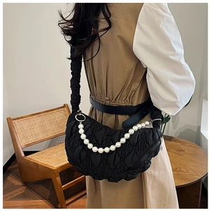 Detail of black quilted croissant bag with pearl chain and pleated texture on model