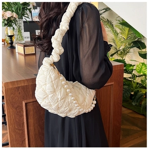 Detailed view of white quilted half-moon bag with elegant pearl chain and pleated strap