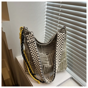 Dettaglio borsa in tela a righe con tracolla geometrica e ciondoli decorativi