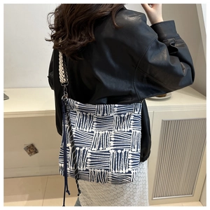 Detail view of woven blue and white checkered tote bag with tassels and wide shoulder strap
