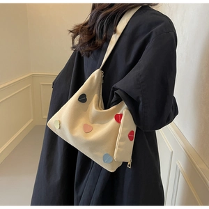 Detail shot of beige canvas tote bag with colorful heart patches and zip closure