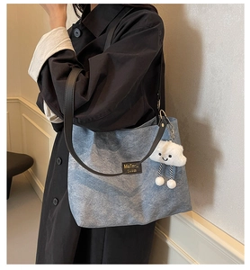 Detail of blue denim tote bag featuring black leather handles and white cloud plush charm