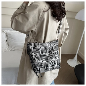 Detail of checkered woven tote bag with fringe accents on a model in beige coat