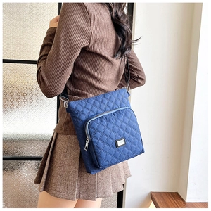 Detail of blue quilted nylon crossbody bag with zipper pocket and metal logo plaque