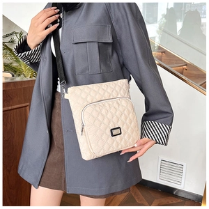 Detail shot of a beige quilted crossbody bag with adjustable wide strap and front zipper