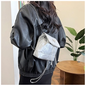 Detail of silver metallic backpack with butterfly buckle and chain strap on black jacket