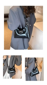 Detail of glossy black shoulder bag featuring a decorative silver metallic bow and knots