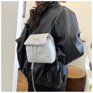 Detail of silver bow logo and chain strap on a metallic trapezoid backpack for women