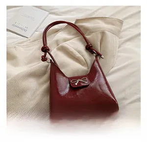 Close-up of a dark red patent leather tote bag featuring a silver metal bow and knotted strap