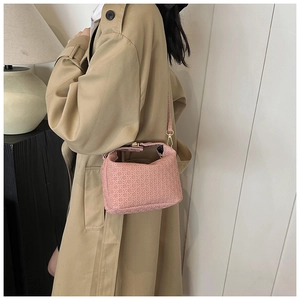 Modern pink woven shoulder bag with gold hardware worn by a model in a trench coat