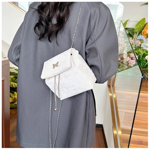 Detail of a white velvet crossbody bag with a silver bow and metal chain strap on a model