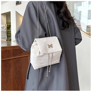 Detail view of cream mini backpack featuring a metallic silver bow and chain strap accents