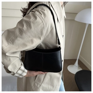 Chic black minimalist underarm bag worn by model featuring fine stitching and slim strap