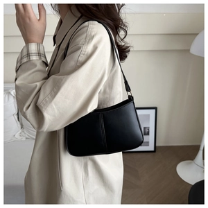 Close-up of minimalist black leather baguette bag with stitch detail and gold hardware