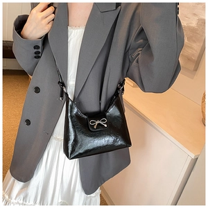 Side view of black glossy underarm bag with silver bow buckle on a gray suit model
