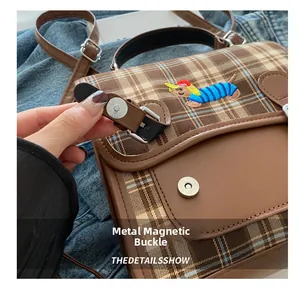 Detail of magnetic snap closure and dachshund embroidery on plaid shoulder bag