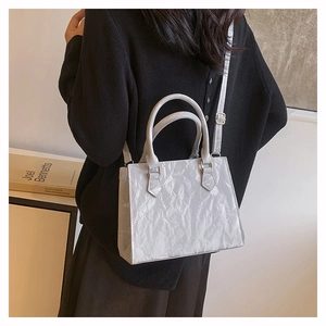 Detail of grey pleated shoulder bag with gold hardware worn on a black knit top