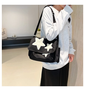 Close-up of black canvas messenger bag featuring white plush star patches and wide strap