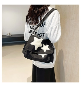 Detail view of black canvas crossbody bag with white plush stars and adjustable strap