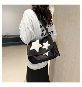 Close-up of black crossbody messenger bag with white plush stars and wide strap