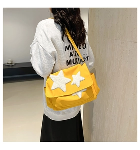 Detail view of yellow canvas messenger bag with white plush stars and wide strap